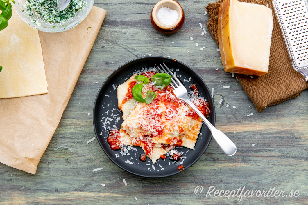 Raviolisar med spenat och ricottafyllning på tallrik med tomatsås och riven parmesan. 