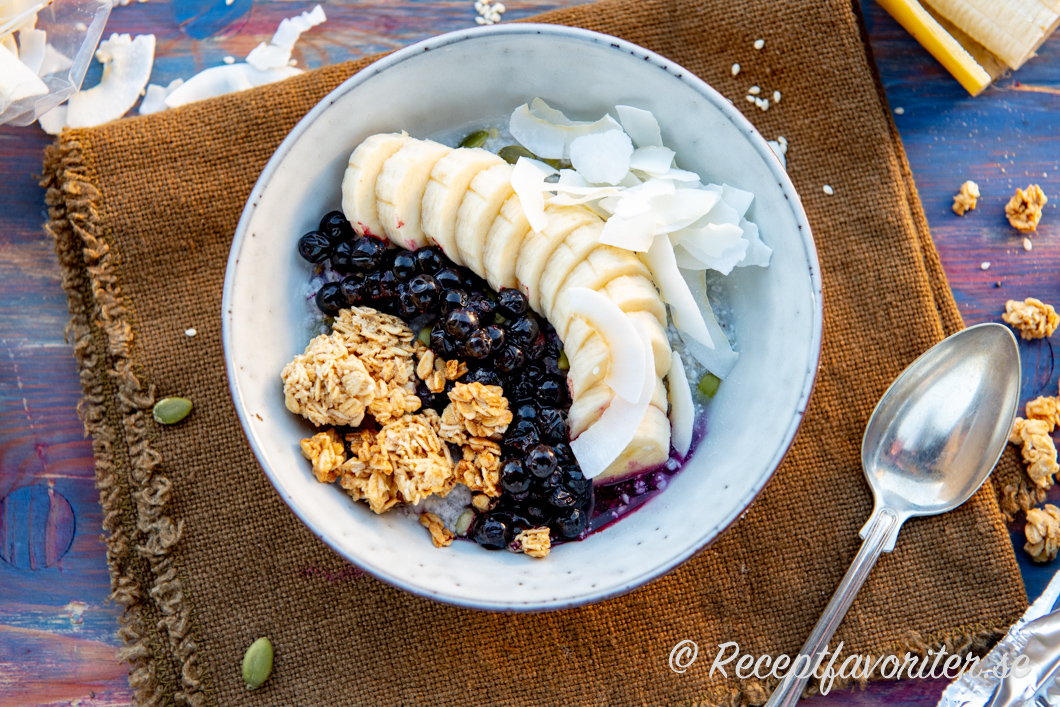 Toppa frögröten med det du gillar. Här med kokosflakes, rårörda blåbär, granola och skivad banan. 