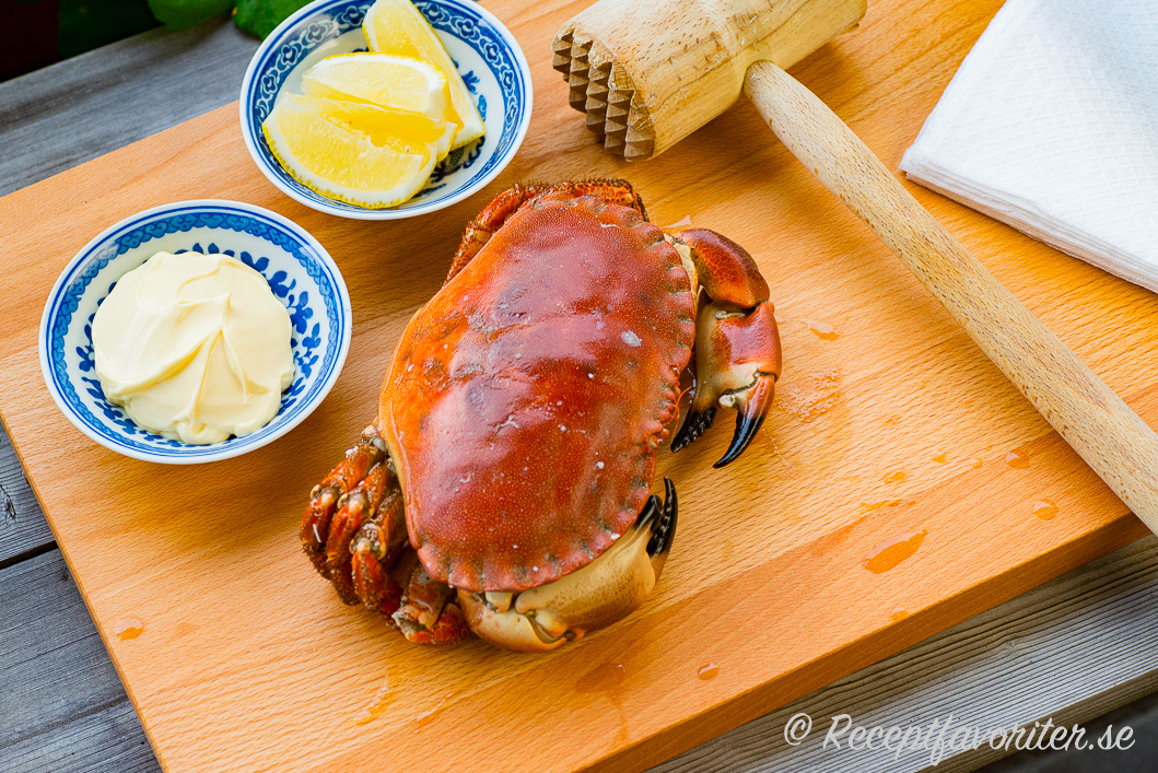Kokt krabba serverad på skärbräda med träklubba, citron och majonnäs samt servett. 