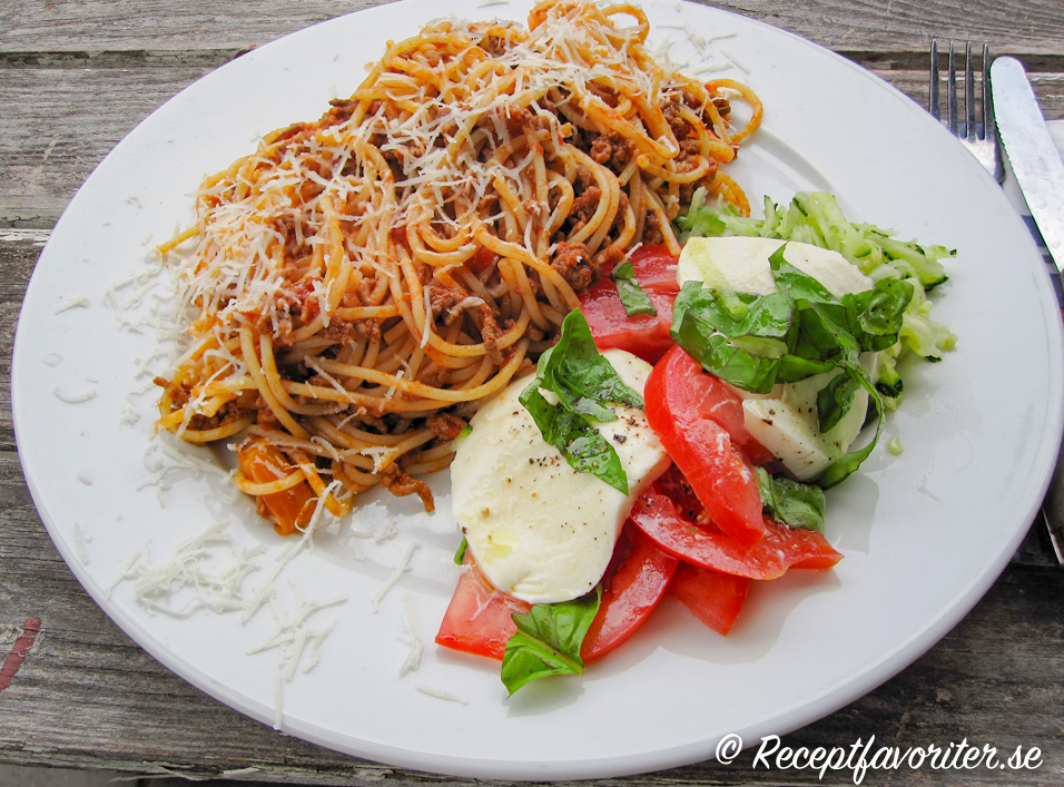 Köttfärssås med spagetti på tallrik med tomat och mozzarellasallad