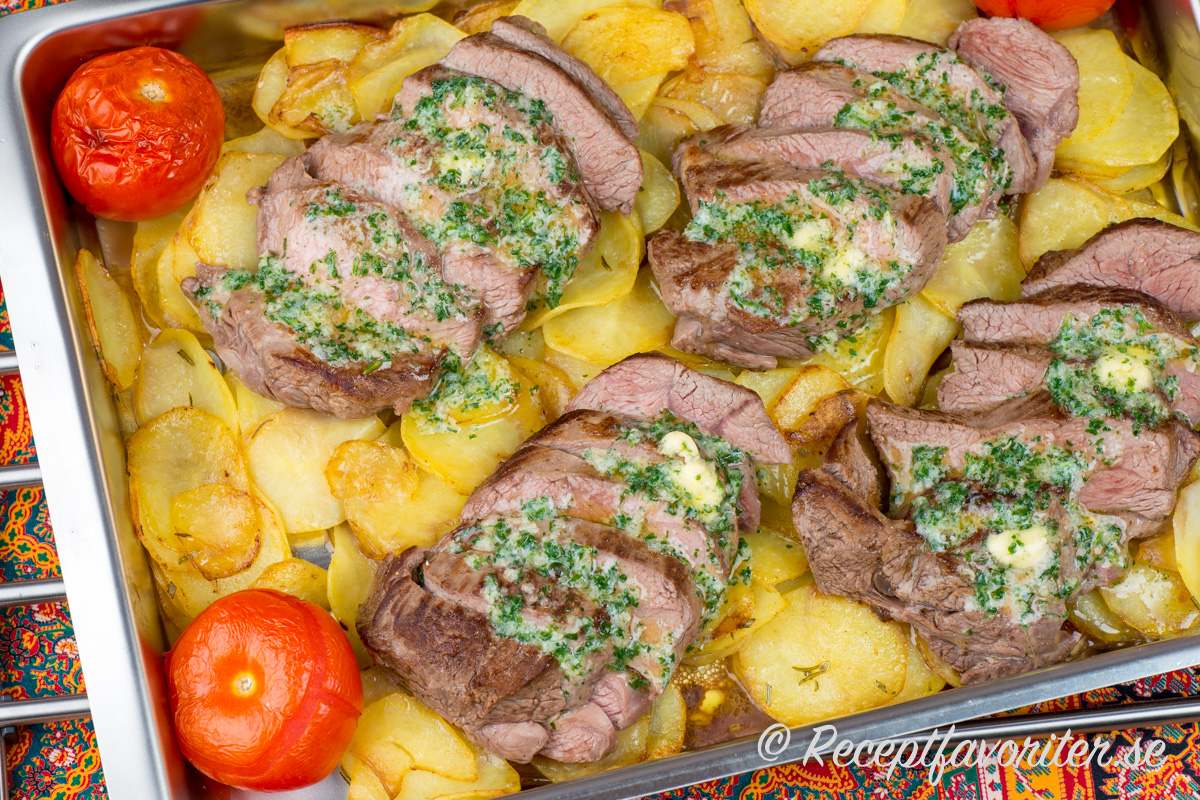 Lammrostbiff med vitlökssmör på en bädd av skivad rostad råstekt potatis och bakade tomathalvor. 