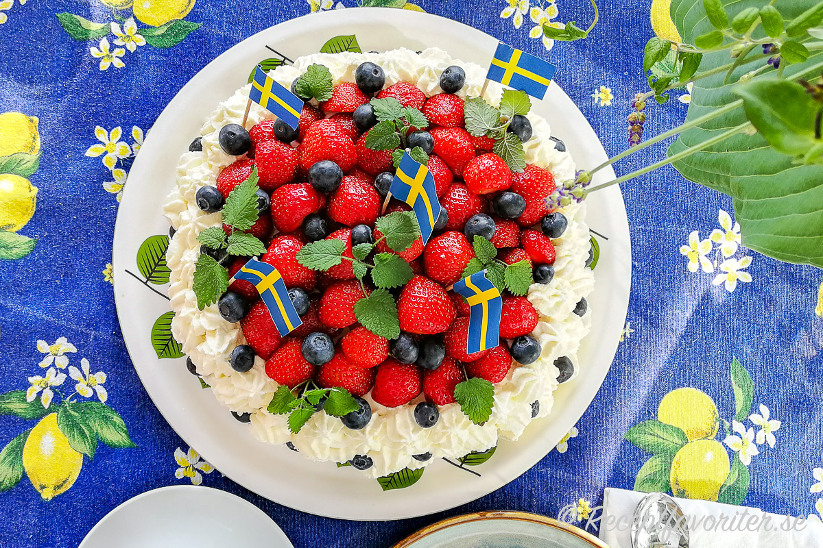 Midsommartårta på midsommarbordet med svenska flaggor och extra blåbär samt citronmeliss. 