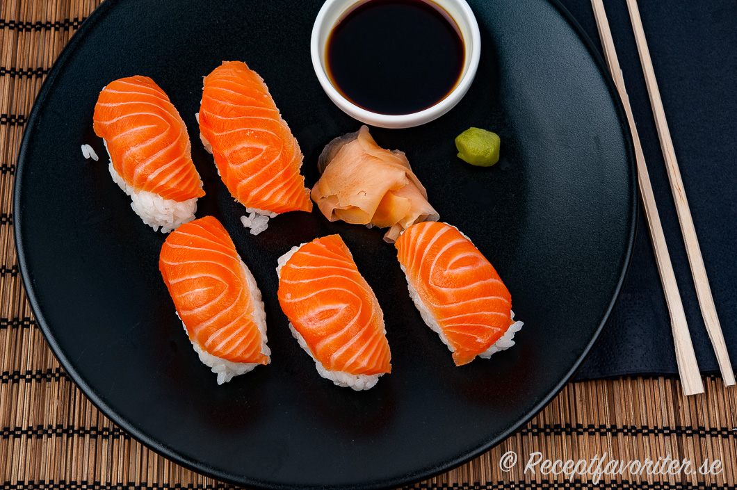 Nigiri sushi med lax och tillbehör på tallrik. 