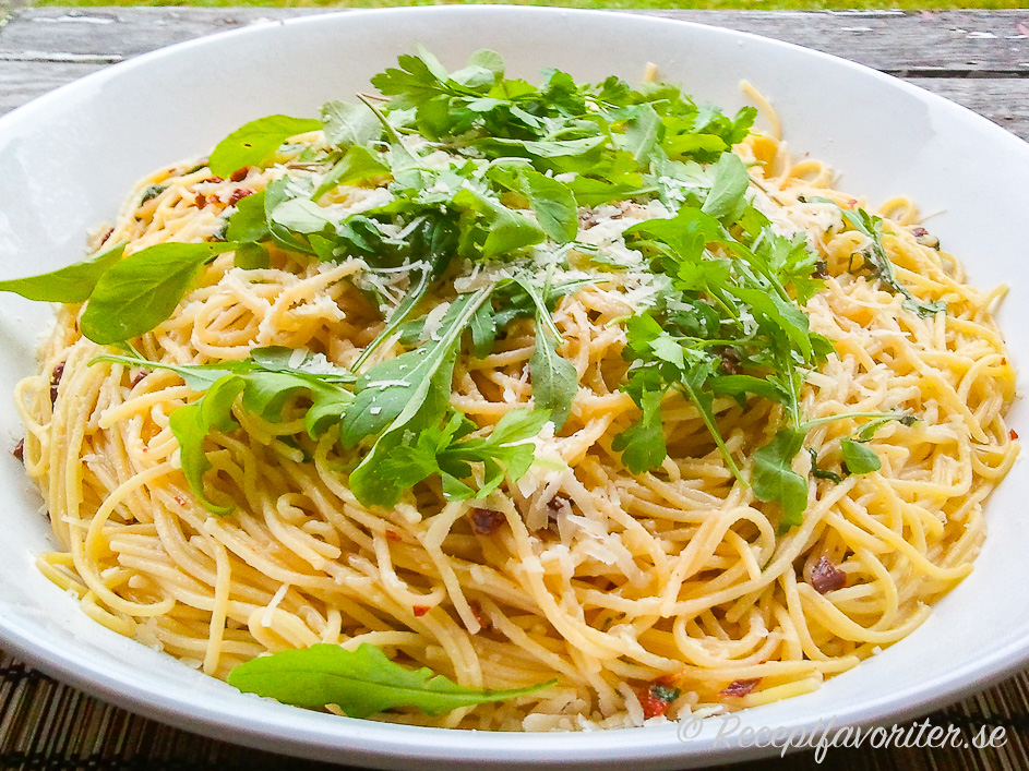 Spagetti på tallrik smaksatt med ruccola, soltorkade tomater och färsk basilika samt riven ost. 
