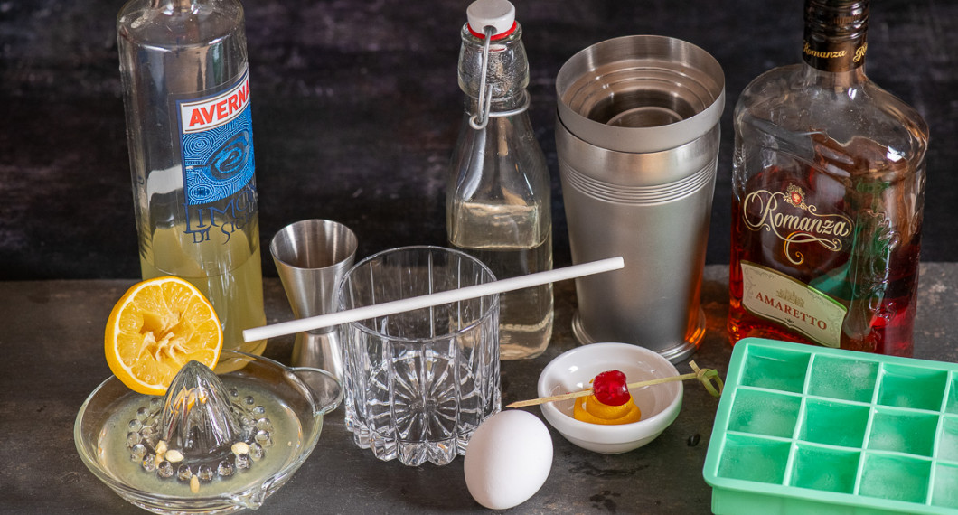Till drinken behöver du Limoncello, citron och citruspress, mätglas, drinkglas, äggvita, sockerlag, garnering av citronskal, cocktailbär och bambupinne, shaker, Amaretto och isbitar. 