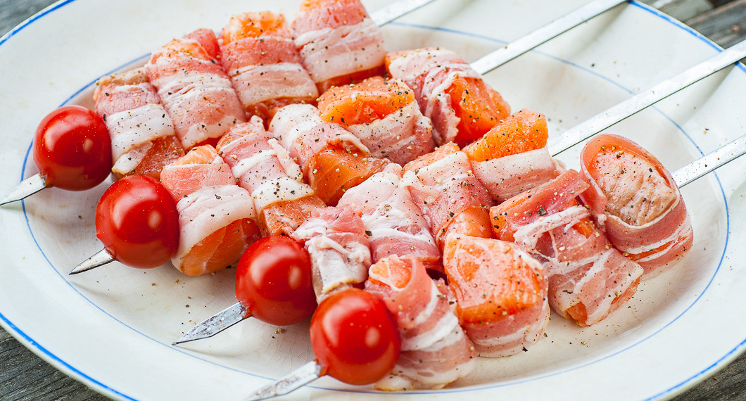 Baconlindad lax på spett med tomat redo för grillen. 