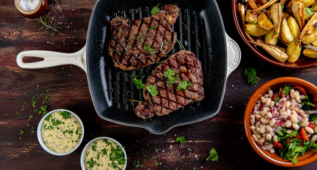 Bearnaisesåsen serverad i portionsskålar garnerade med hackad kruspersilja till grillad entrecote, klyftpotatis och marinerade vita bönor. 