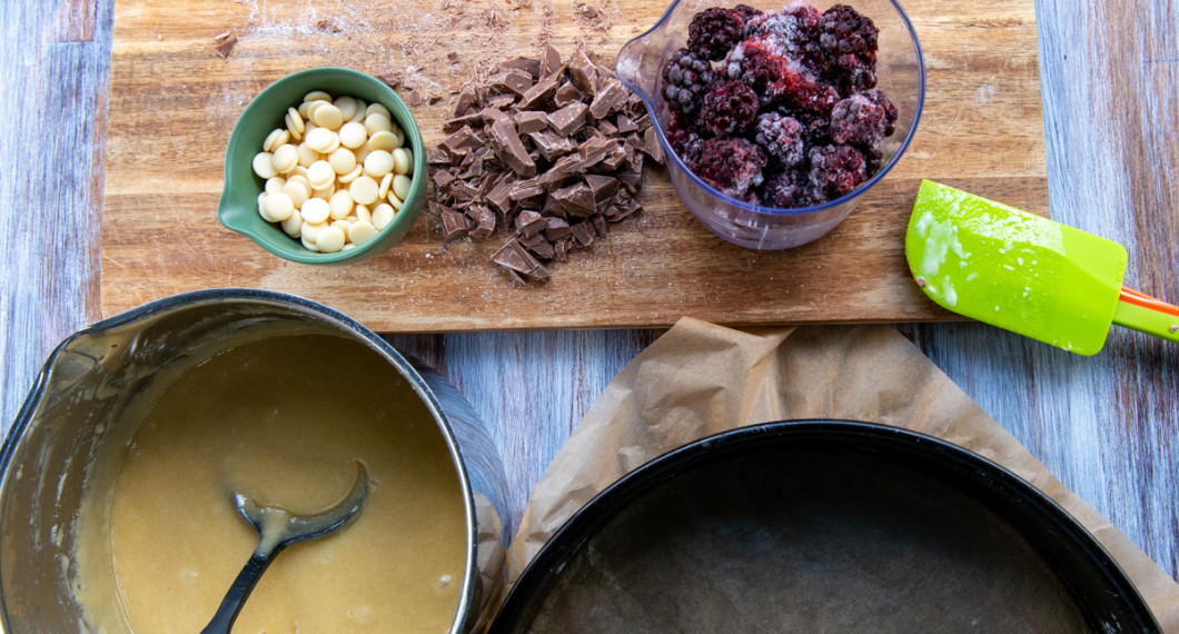 Sätt på ugnen, förbered smet med vit choklad i samt ta fram en rund springform med bakplåtspapper i botten, vita chokladknappar, hackad mjölkchoklad samt björnbär. 