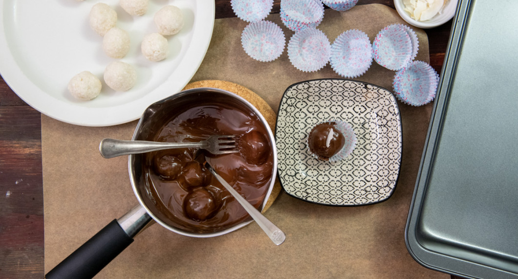 Frys kokosbollarna och doppa dem sedan i smält choklad samt lägg i knäckformar eller på bakplåtspapper att stelna. 