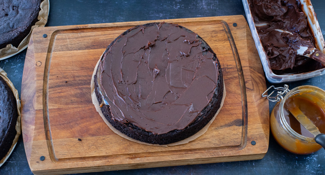 Bred ut fyllningen av kolasås och chokladkolaglasyr på varje lager av tårtbotten. 