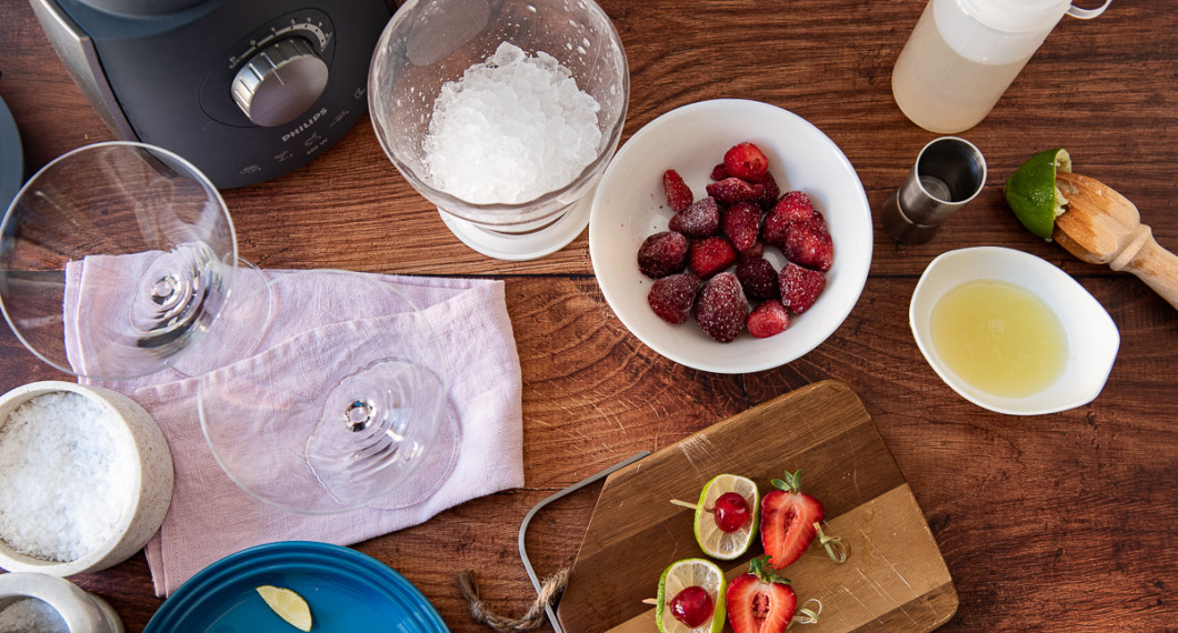 Ingredienser till jordgubbsmargaritan: frysta jordgubbar, limesaft, sockerlag, krossad is och så garnering av lime, cocktailbär och jordgubbshalva på bambupinne. Utanför bild tequila och apelsinlikör. 