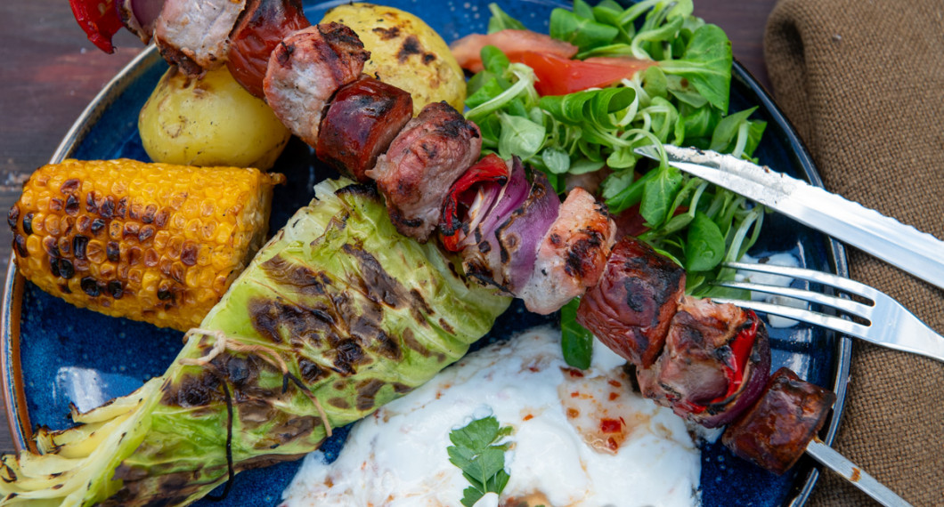 Grillad spetskål serverad med grillad majs, grillad potatis och grillspett med fläskfilé och korv. 