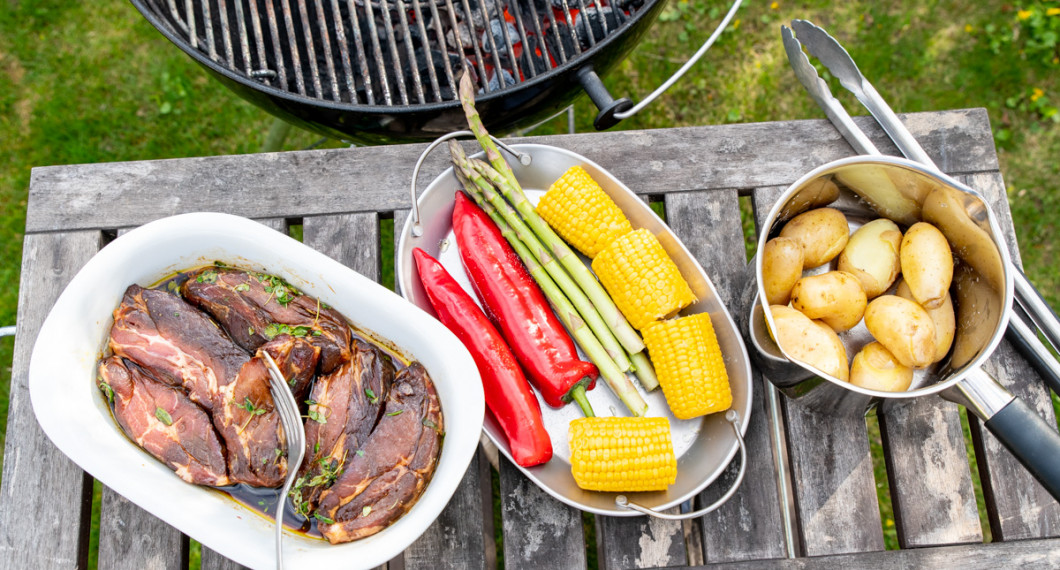 Ingredienser redo för grillen: vildsvinskarrén i marinad; ett fat grönsaker och kokt potatis. 