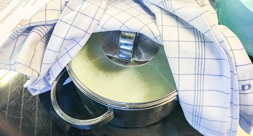 Mjölken står och ystar i kastrull under handduk så den håller värmen. 