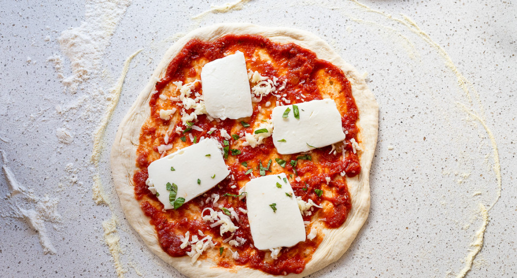 Lägg på toppings. Först tomatsås, sedan riven ost samt mozzarellaost och färsk basilika för en margarita. 