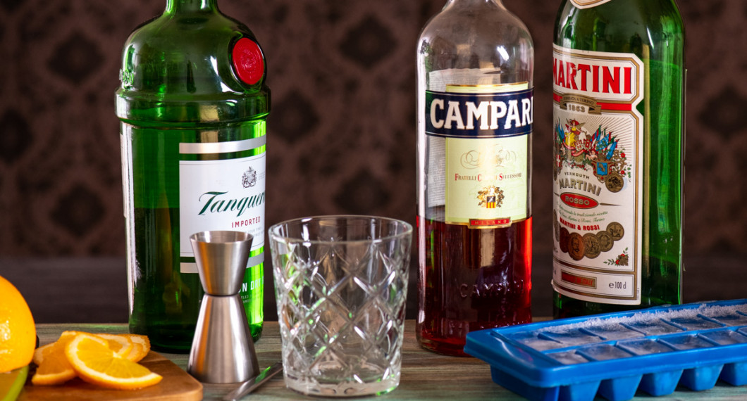 Ingredienser till Negroni: gin, campari och röd vermouth. Vidare apelsin till garnering, cl mått, drinkglas och is.  