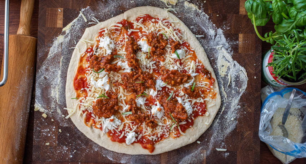 Pizzabotten toppas med tomatsås, riven mozzarella, köttfärssås samt klippt färsk rosmarin. 