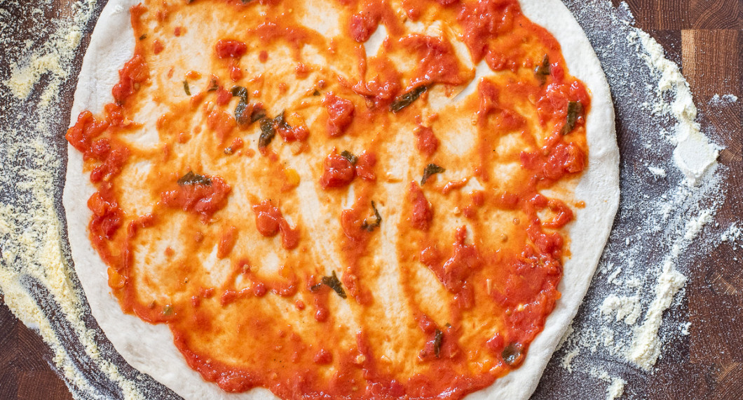 Pizzasåsen breds ut i ett tunt lager på pizzabottnen. 