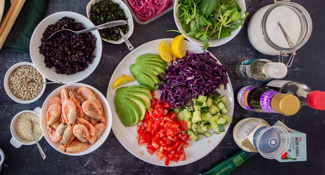 Ingredienser till pokebowlen: hela räkor, rostade sesamfrön och solrosfrön; kokt svart råris, rostad sjögrässnacks, picklad rödlök, späd grönsallad, avokado, rödkål, tomat, gurka samt chili, sesamolja och citron till marinad; socker, risvinäger, soja, majonnäs och wasabi till dressing.  