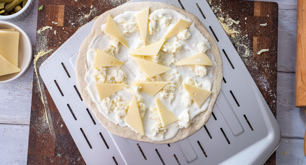 Pizzabottnen får först ett tunt lager crème fraiche. Sedan fördelas riven mozzarella och racletteost över. 