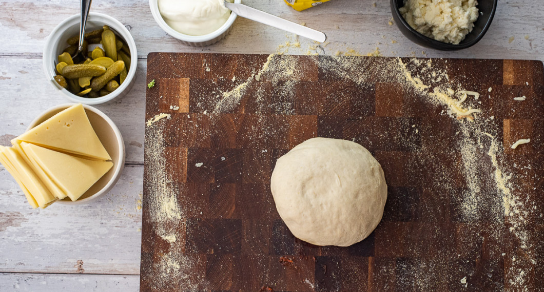 Ingredienser till raclettepizzan: racletteost, cornichons, crème fraiche, majsmjöl till utbakning, pizzadeg samt mozzarella. 