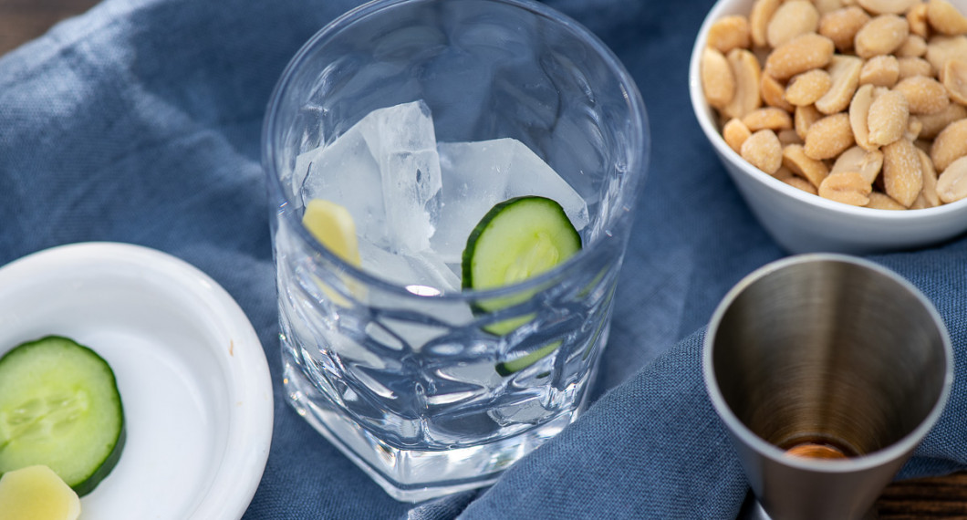 Lägg isbitar samt skivor av gurka och färsk ingefära i ett lågt drinkglas. 