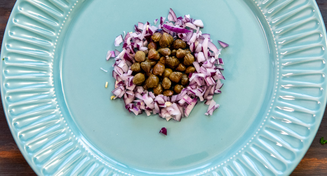 Lägg en cirkel med kapris i mitten på en förrättstallrik. Lägg rödlök runt i en ring. 