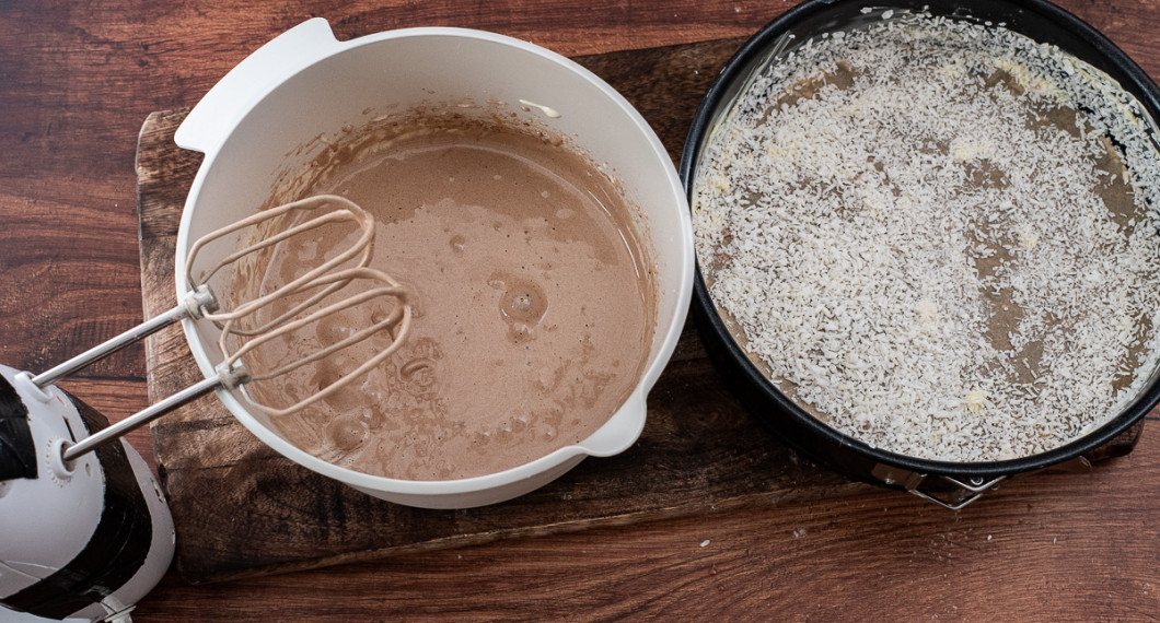 Vispa i de torra ingredienserna samt smält smör till en smet. Smörj och bröa en rund springform med bakplåtspapper i botten med lite smör och kokosflingor eller ströbröd. 