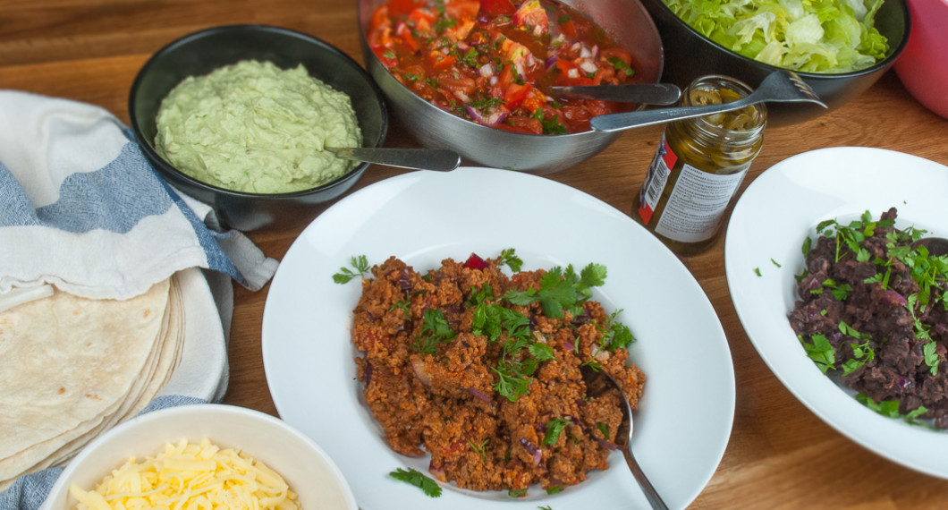 Varma tortillabröd, guacamole, tomatsalsa, isbergssallad, riven ost, tacofärs (köttfärs för de som vill ha det) och stekta mosade svarta bönor. 