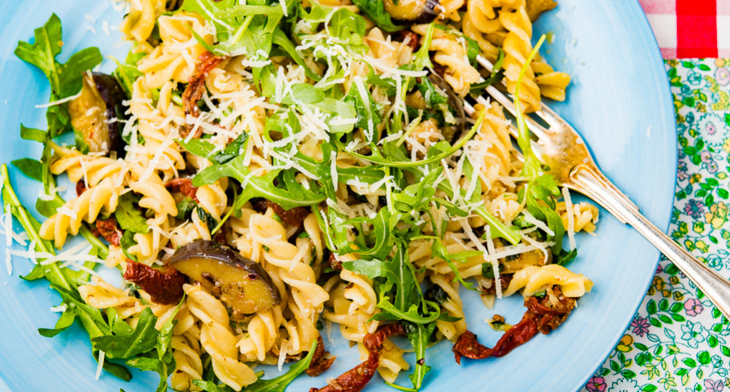 Vegetarisk pasta på tallrik garnerad med riven ost och ruccola