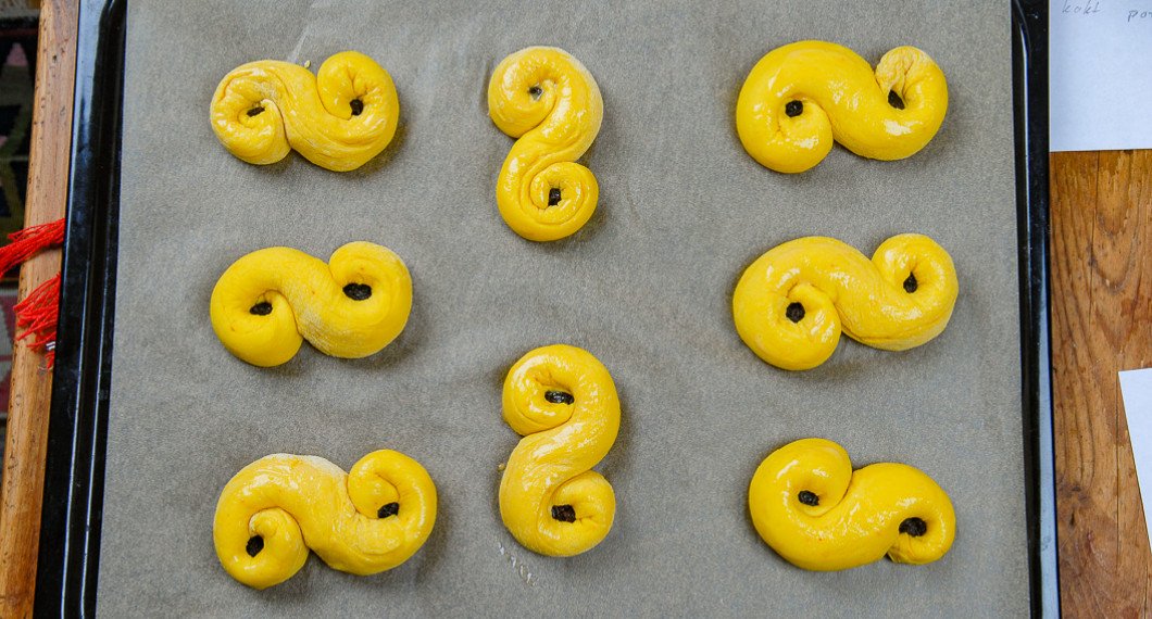 Lussekatterna får en andra jäsning på bakplåtspapper innan de gräddas i ugnen. 