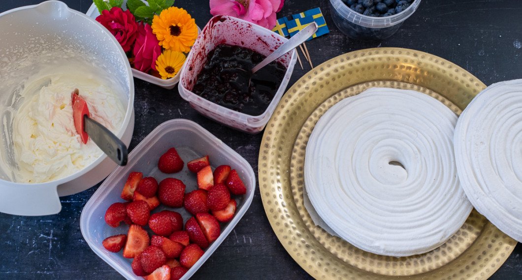 Ingredienser till marängtårtan: Vispad grädde, jordgubbar, blommor, sylt, blåbär samt marängbottnar. 