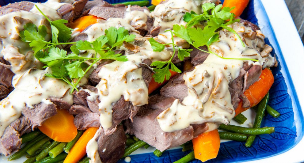 Uppskuren rådjurssadel lagd på fat toppad med kantareller, tillbehör och persilja