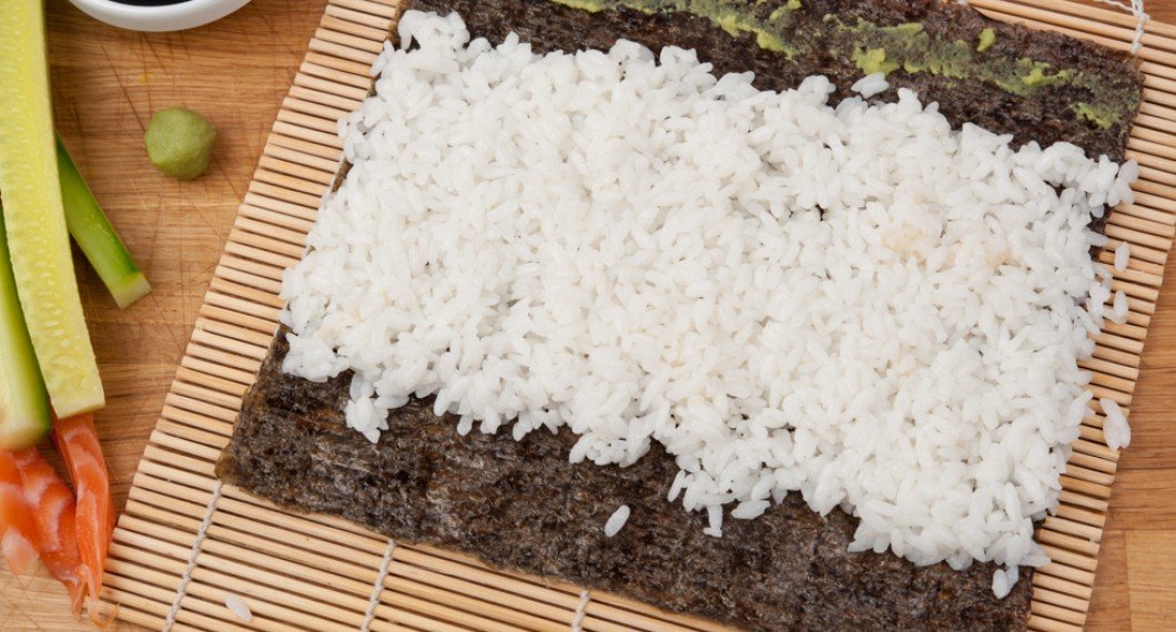 Kokt sushiris på ett blad sjögräs - nori - som rullas till maki rulle. 