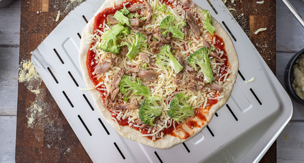 Pizzan toppas med tomat- pizzasås, riven mozzarella, färsk mozzarella, broccoli, kycklingkött och bakas sedan. 