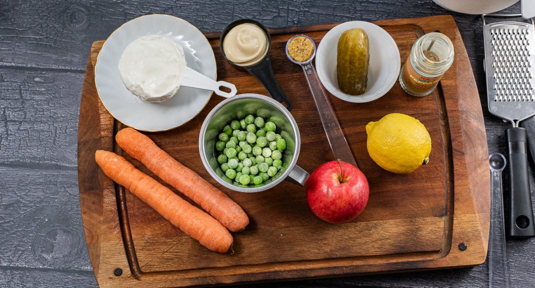 Till salladen behöver du morötter, gräddfil, majonnäs, gröna ärtor, senap, äpple, saltgurka, citron och vitpeppar. 