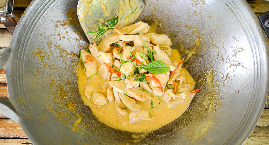 Kycklingen wokas och blandas med kokosmjölk och smaksättning i woken. 