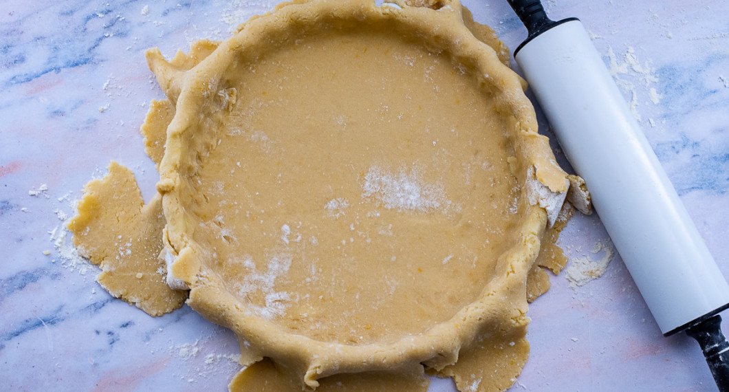 Rulla upp degen på kaveln och rulla ut den över pajformen. Forma och tryck till degen runt kanterna. 