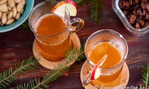 Två glas varm äppeldrink med must, sprit som bourbon, citron och kanel garnerad med en skiva äpple. 