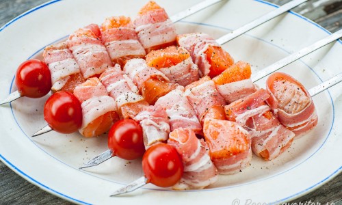 Baconlindad lax på spett med tomat redo för grillen. 