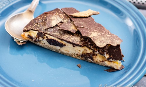 En bit biskvitårta med mandelbotten och smörkräm toppad med ett lager choklad samt bitar av choklad med guldpulver som dekor. 