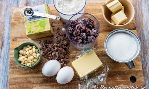 Ingredienser till kakan: vita chokladknappar, vaniljsocker, ägg, mjölkchoklad, smör, vetemjöl, färska eller frysta björnbär, socker och vit choklad. 