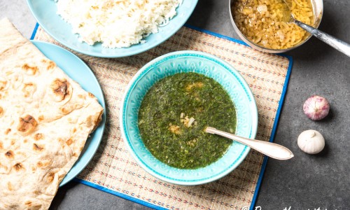 Egyptisk grönsaksgryta eller tjock soppa Molokhia eller Mulukhiyah serverad med arabiskt bröd, ris och lök, vitlök och chili fräst i olja.