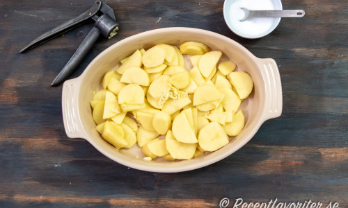 Lägg skivad potatis i en gratängform och tillsätt pressad vitlök och salt. 
