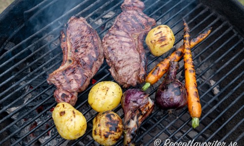 Ryggbiffen på grillen med grönsakstillbehör som potatis, knippmorötter och rödlök. 