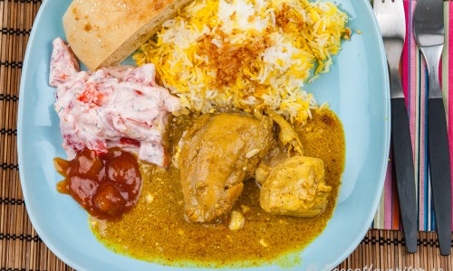Indisk currygryta med kycklingdelar på tallrik med tillbehör
