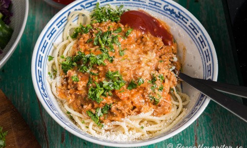 Köttfärssås med spagetti toppad med riven parmesan och hackad persilja samt ketchup vid sidan. 