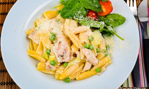 Kycklingfilé med pasta, parmesan och ärtor på tallrik med lite grönsallad