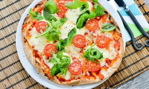 Libapizza med mozzarella, basilika, ruccola och tomat på tallrik