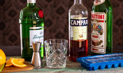 Ingredienser till Negroni: gin, campari och röd vermouth. Vidare apelsin till garnering, cl mått, drinkglas och is.  
